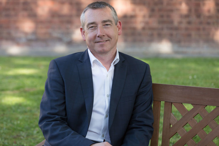 Man in suit sitting on a wooden bench in a garden
