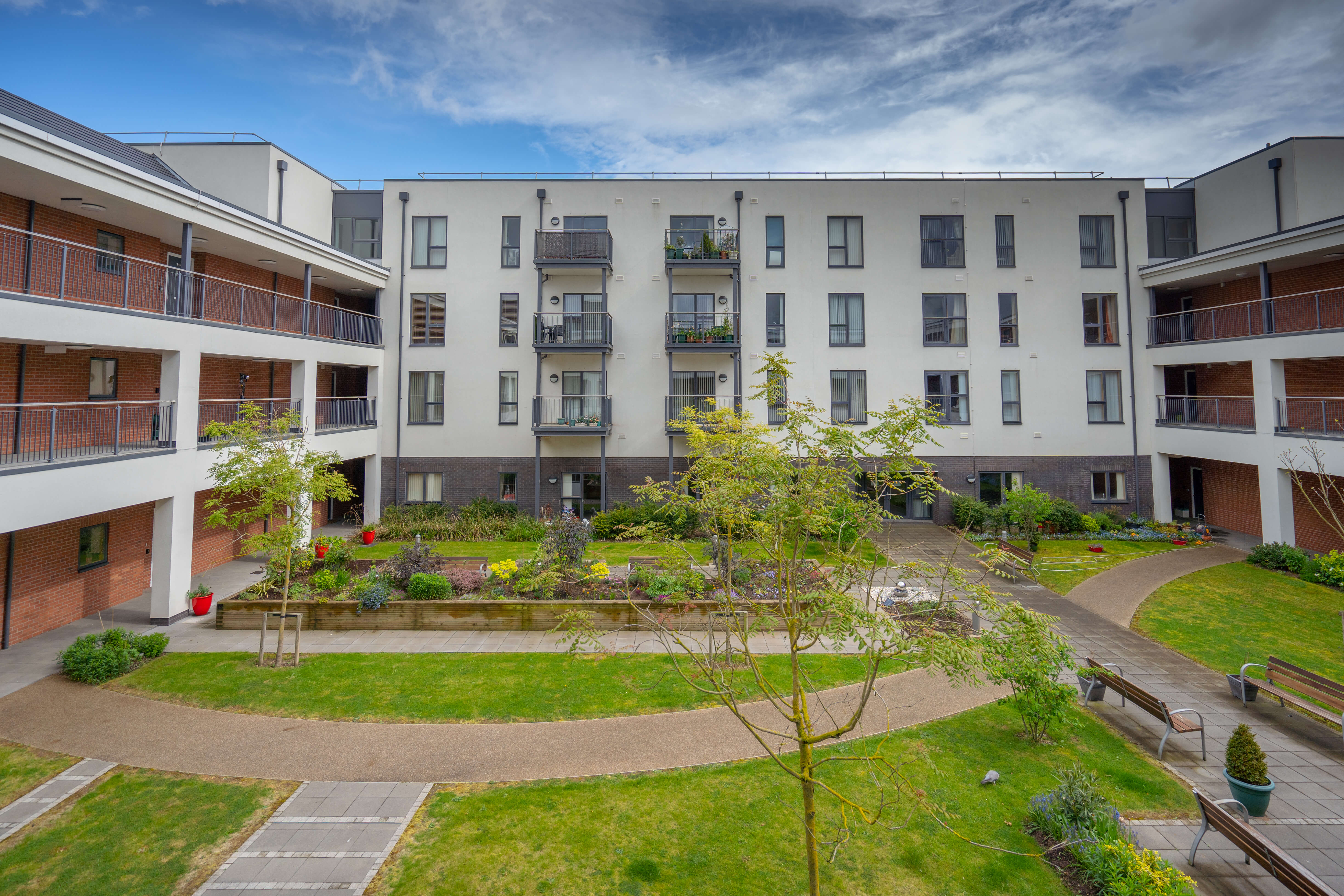 U-shaped apartment block with a lawn with trees, pathways and benches in the centre of the building