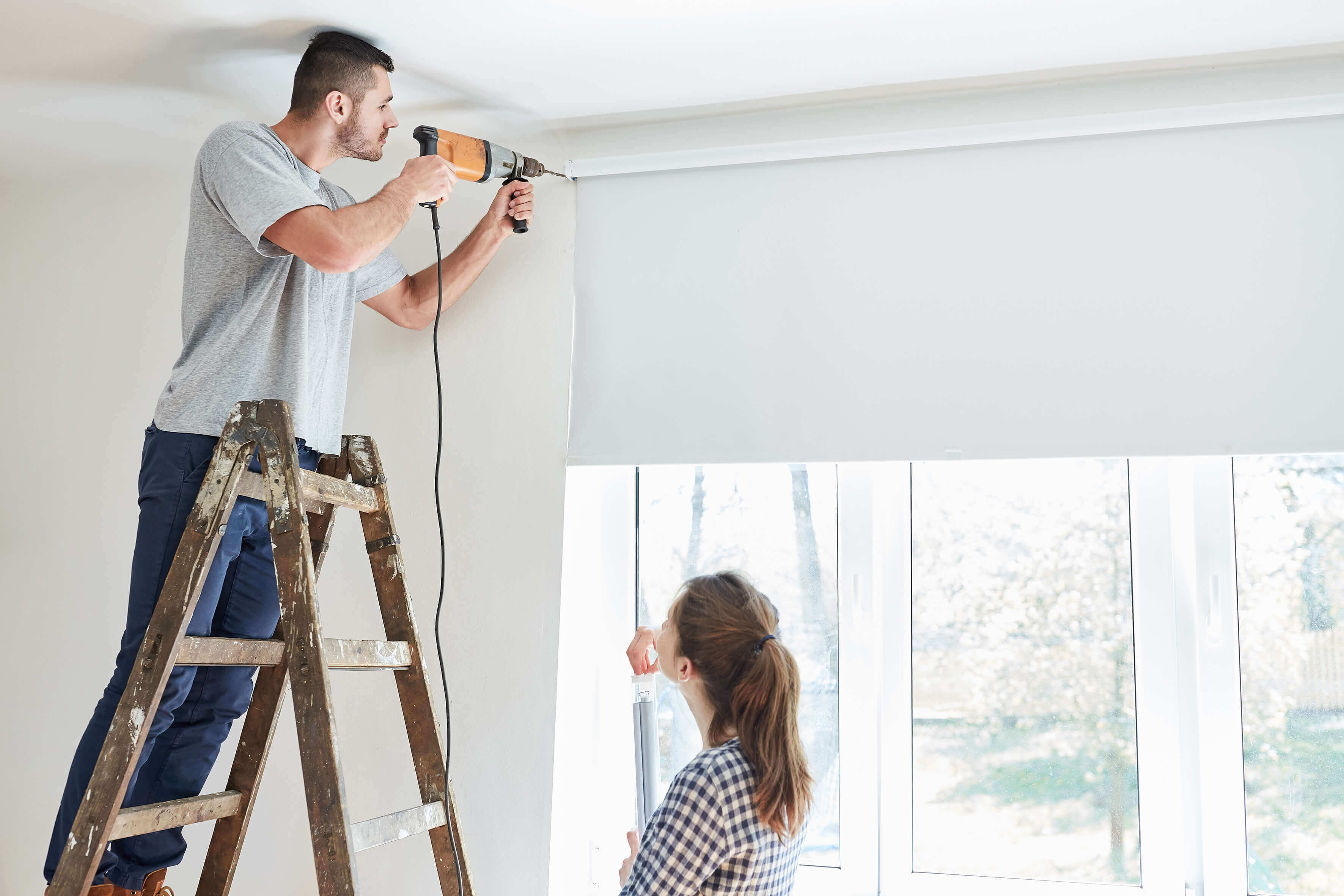 man on ladder drilling into wall
