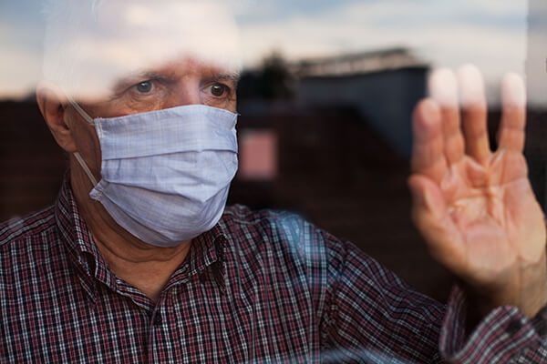 man touching window and looking out wearing a mask