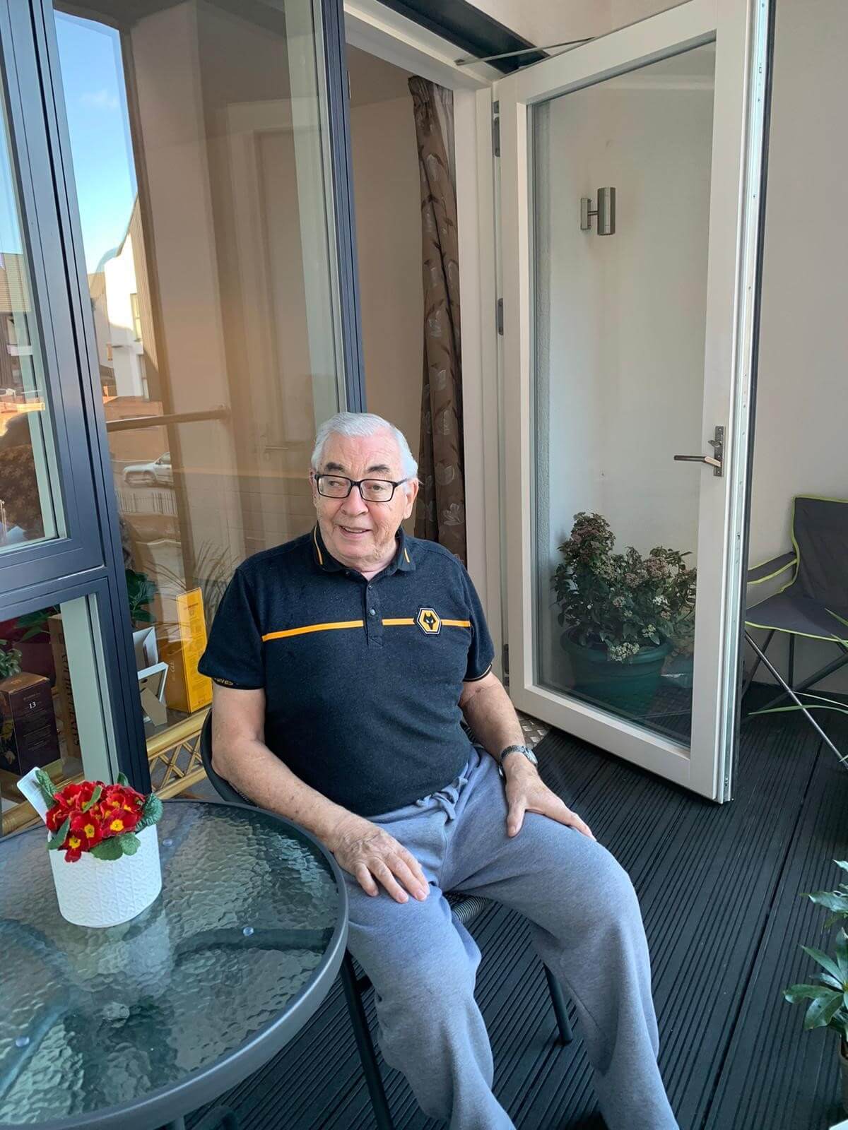 Older gentleman sitting on a chair at the glass table on his house patio
