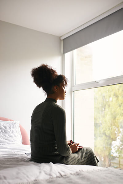 woman sitting on her bed looking out the window
