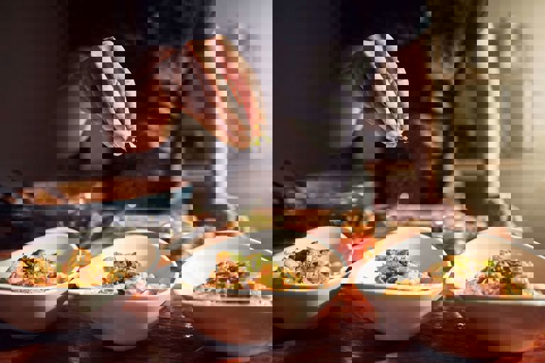 Hand drizzling herbs on food in a bowl