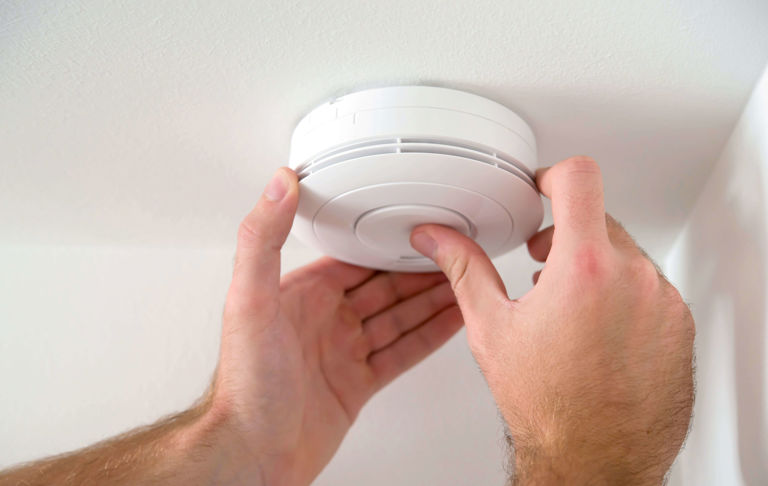 hands installing a carbon monoxide alarm on ceiling