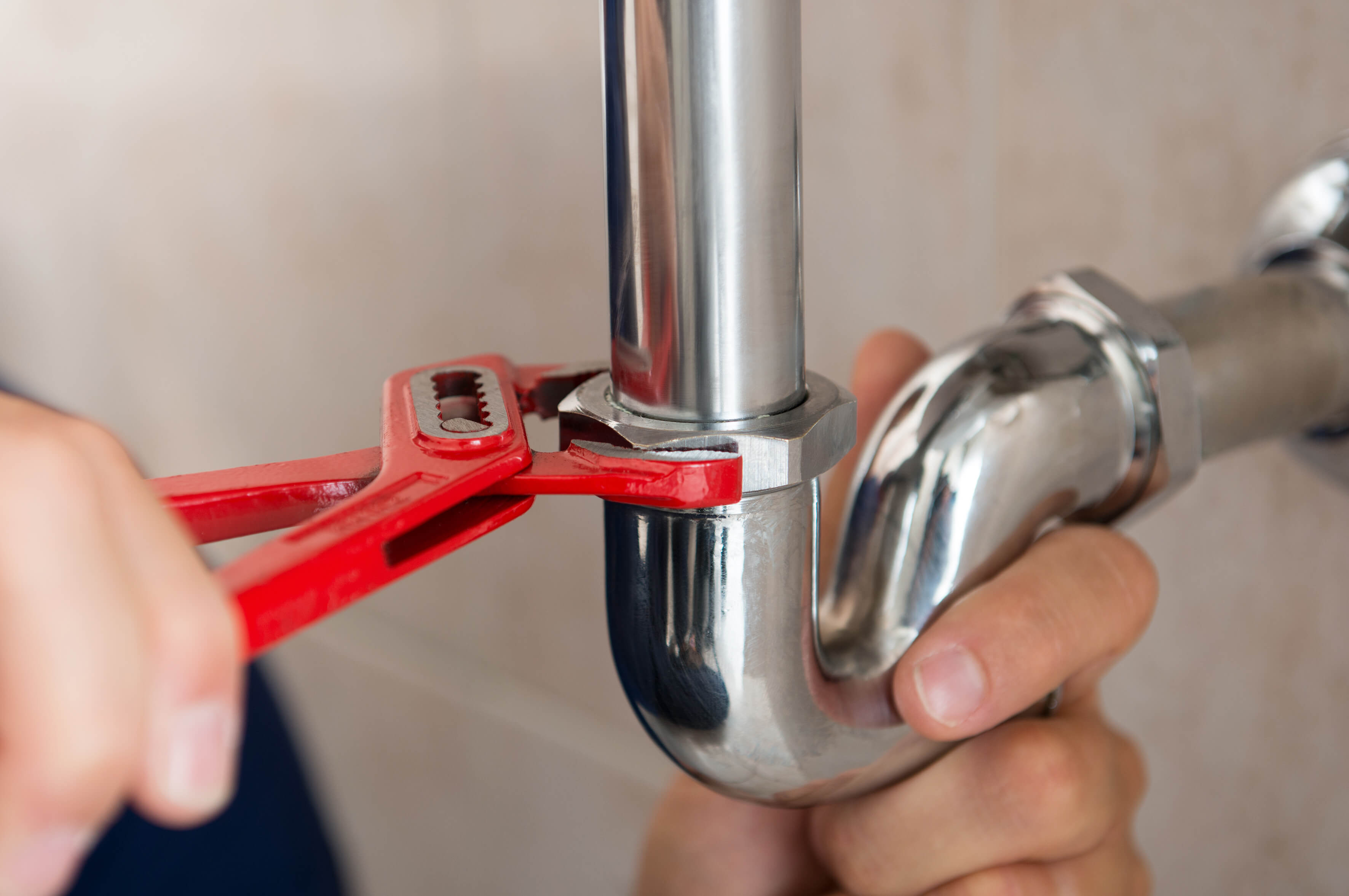 Hand fixing a silver pipe with a red spanner