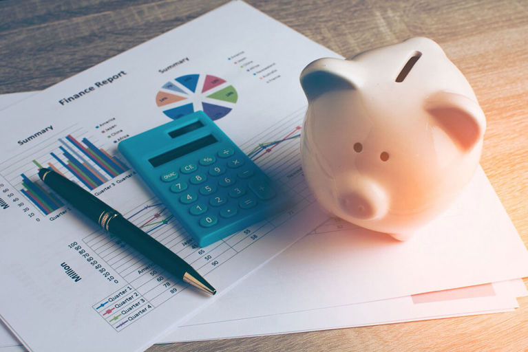 piggy bank next to a calculator and pens on pieces of paper