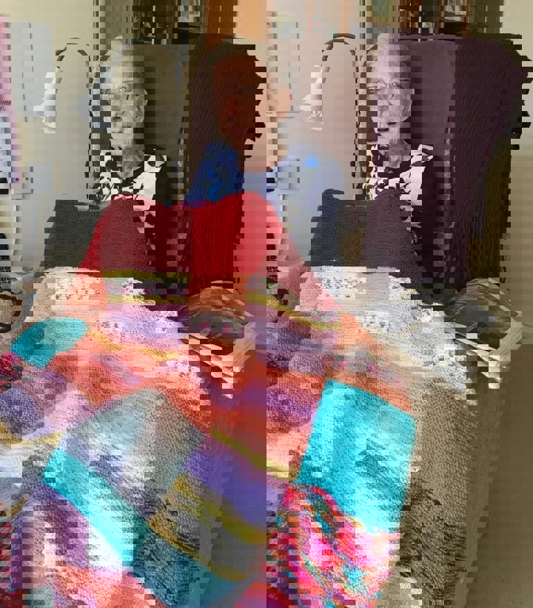 Elderly lady sitting under a colourful blanket