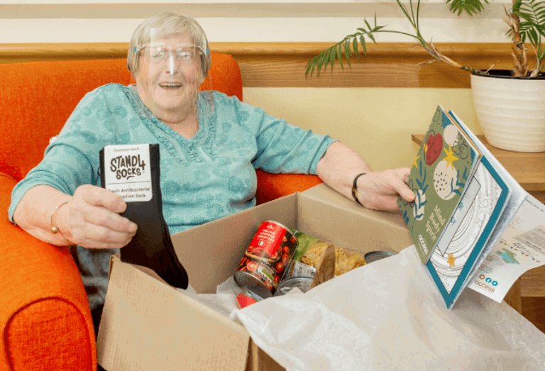 Elderly lady opening a care box filled with socks, can and books
