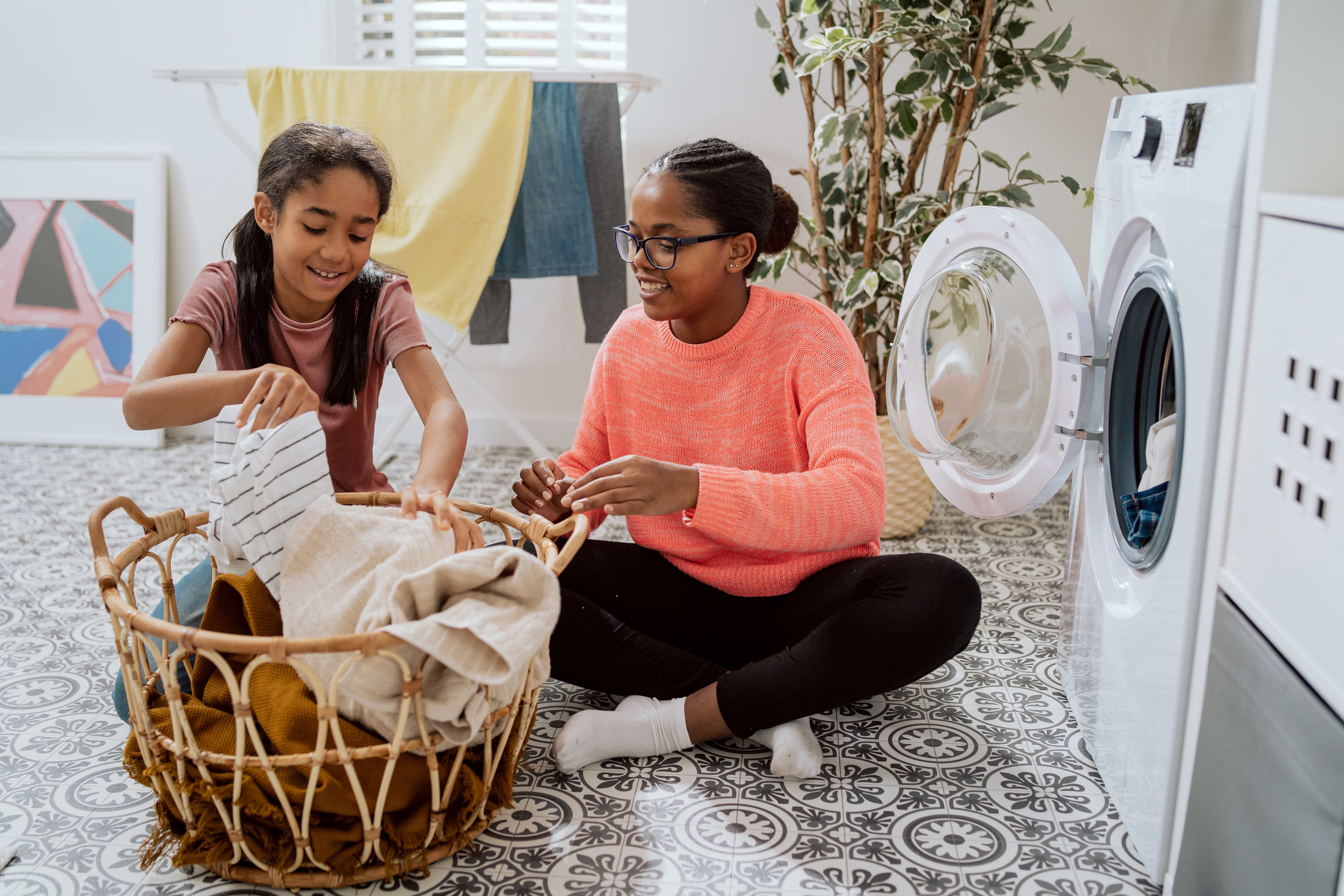 Two girls sat on the floor putting clothes into a washing machine